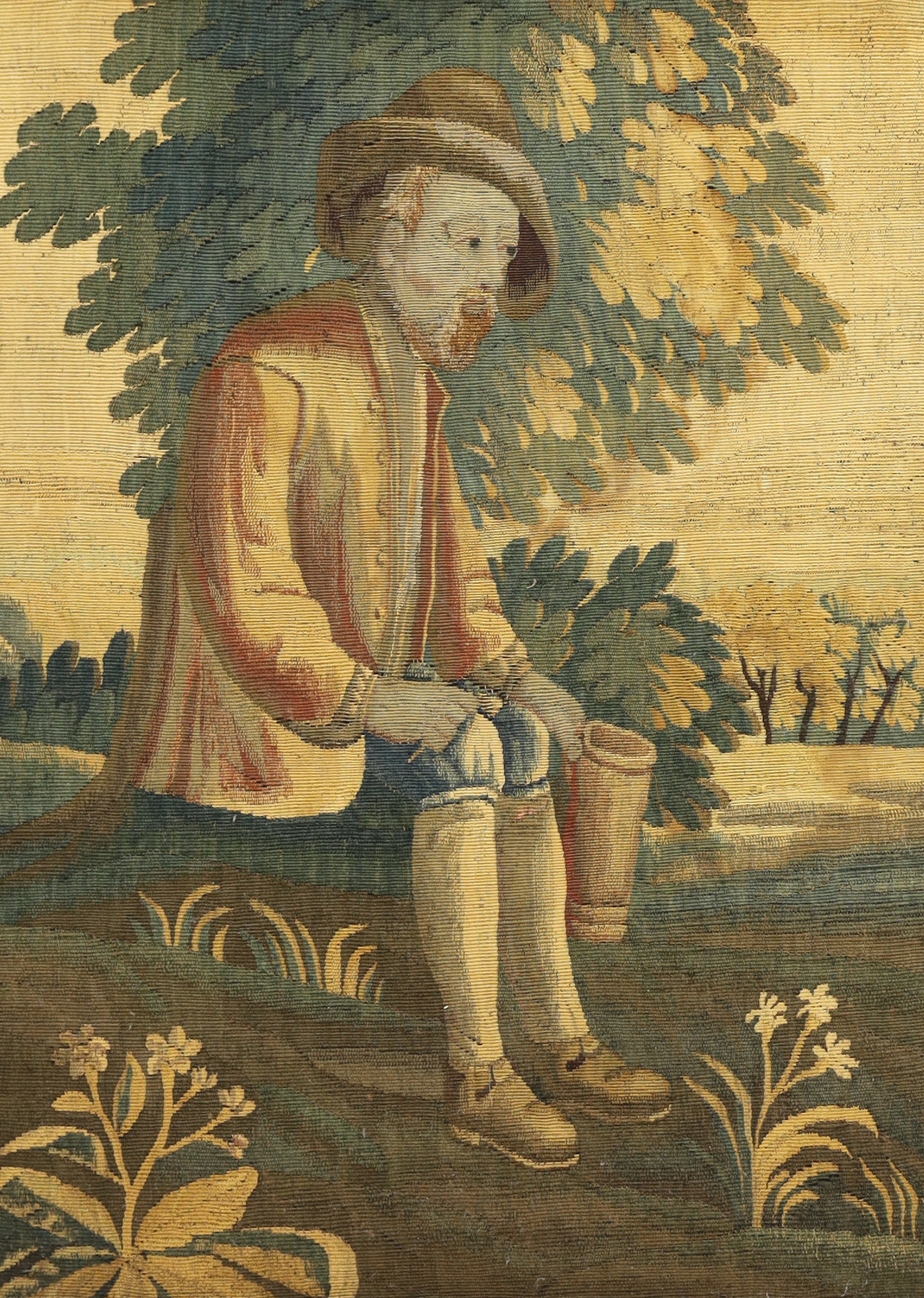 Two 18th century Brussels verdure tapestry panels, one of a seated peasant lady holding a flagon and the other a similar gentleman holding a large tankard, surrounded by lush green landscape, probably part of a larger ta